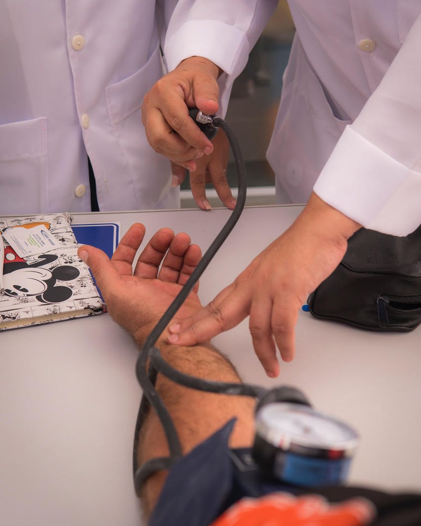 Aula prática na Abazze Técnica: aluna afere a pressão arterial de um colega, localizando o pulso antes de insuflar o manguito