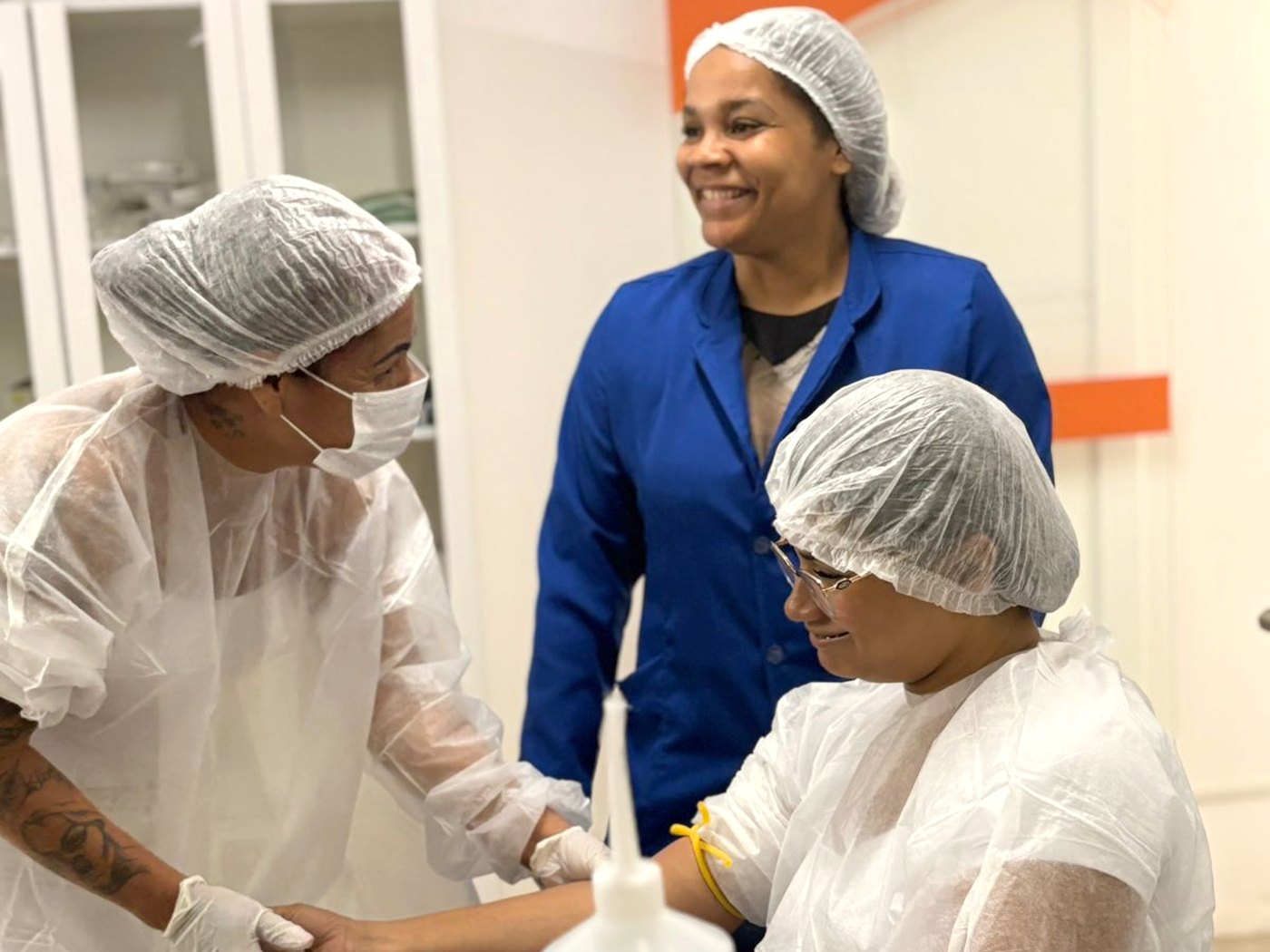 Aula prática de punção venosa no laboratório da Abazze Técnica: aluna realiza o procedimento em colega, acompanhada pela professora